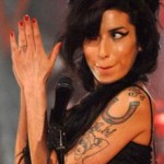 Tatouage d'Amy Winehouse sur le bras : pin up aux seins cachés et fer à cheval