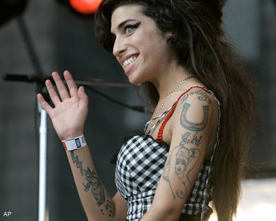 Tatouage d'Amy Winehouse sur le bras : pin up seins nus et fer à cheval