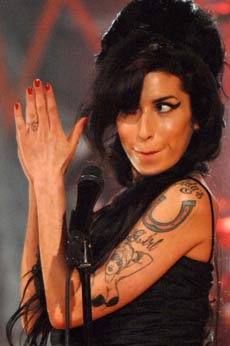 Tatouage d'Amy Winehouse sur le bras : pin up aux seins cachés et fer à cheval